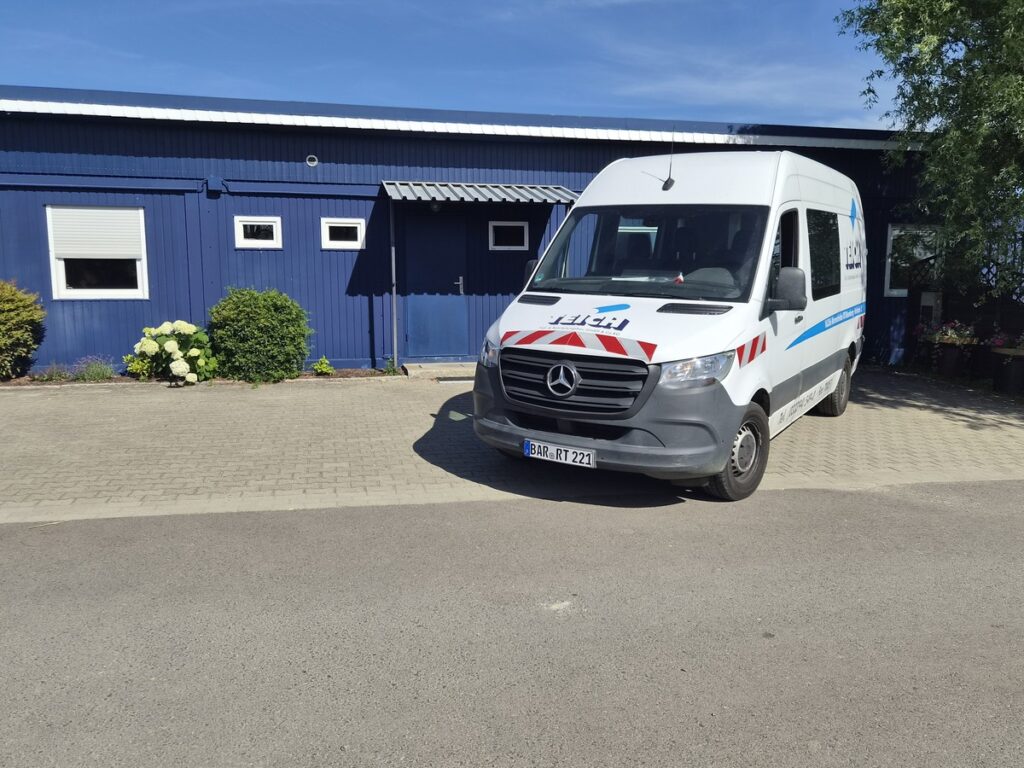 Weisser Mercedes Transporter mit rotblauen Streifen vor blauem Gebäude