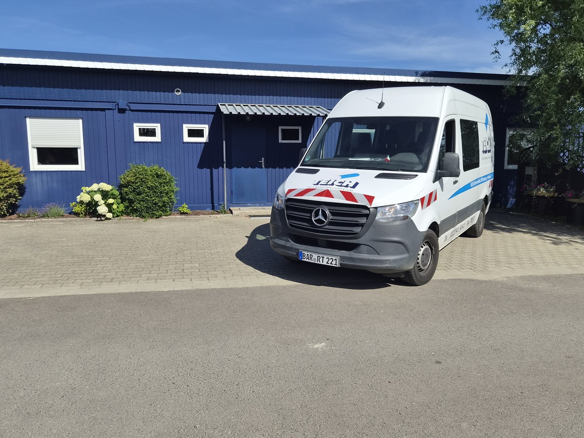 Weisser Mercedes Transporter mit rotblauen Streifen vor blauem Gebäude