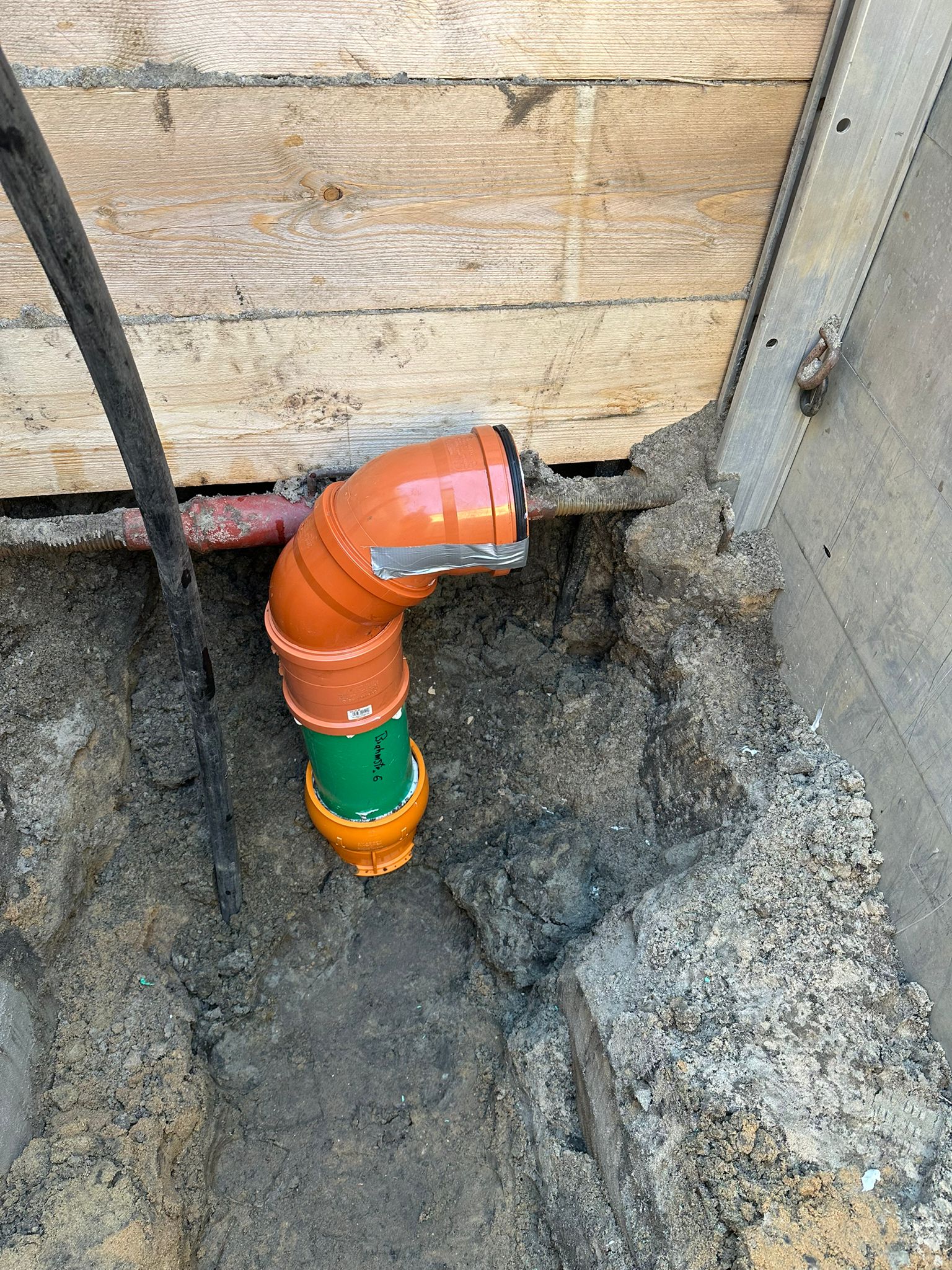 Orange gruene Rohrverbindung mit silbernem Band in schlammiger Baugrube