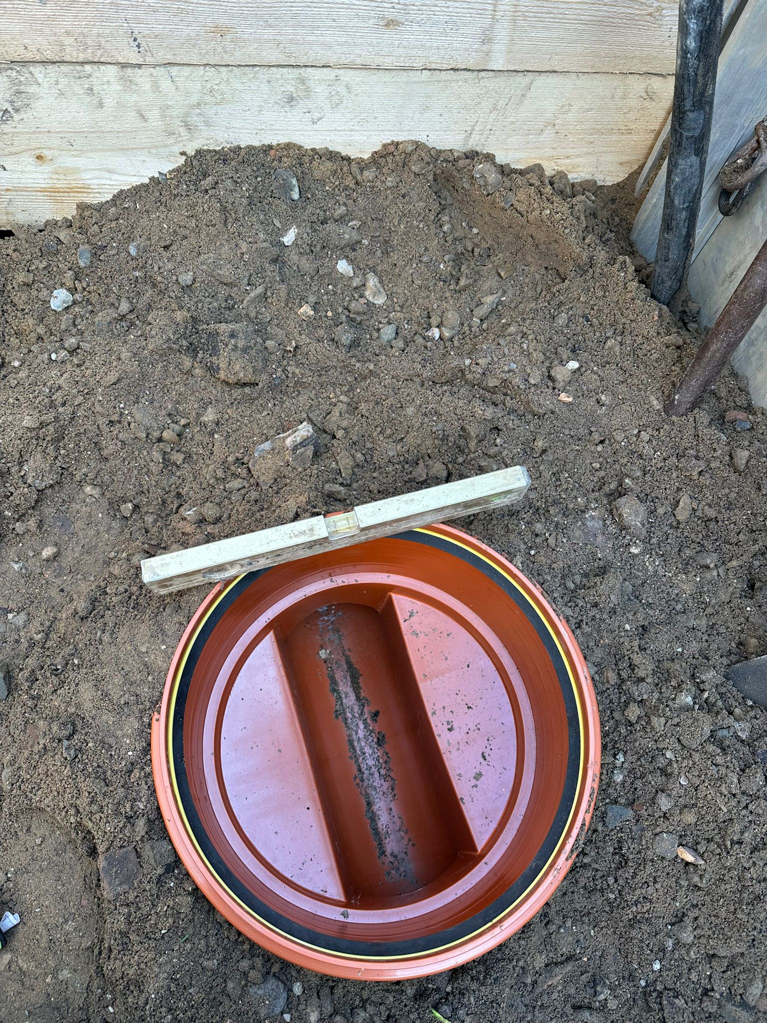 Braune Erde und roter runder Schachtdeckel mit Wasser und Messstab