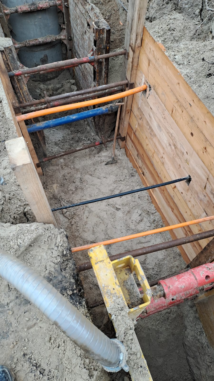Baugrube ohne Personen mit Holzverschalung und bunten Stahlstreben in Grau